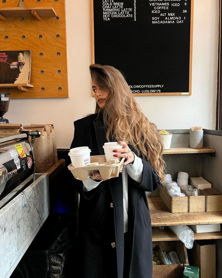 324de386-b570-4de7-9c36-2a90c8dc2380 Woman holding coffee tray in cozy café with menu board in background. | Sky Rye Design Woman holding coffee tray in cozy café with menu board in background.