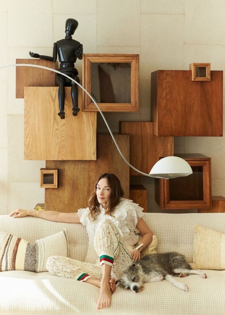 Woman sitting on couch with dog, modern decor and artistic mannequin in background. Cozy living room scene.