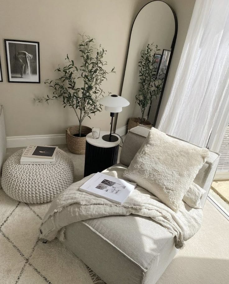 Cozy modern living room with a lounge chair, knit pouf, large mirror, and indoor plants, bathed in natural light.