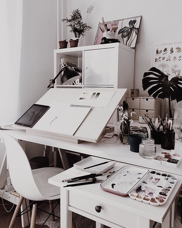 Home office with art supplies and plants on a white desk and chair setup.