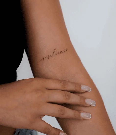 Delicate resilience tattoo on an arm, showcasing minimalist script design and personal empowerment.