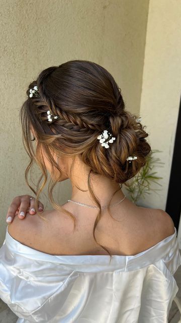 Elegant bridal updo with braid and floral accents, woman in off-shoulder gown, perfect for weddings.