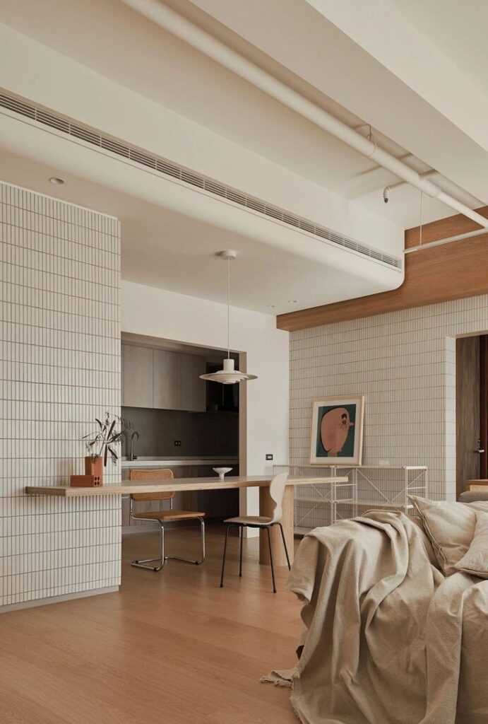 Minimalist open-plan living room and kitchen with modern furniture and artwork, featuring neutral tones and wooden flooring.