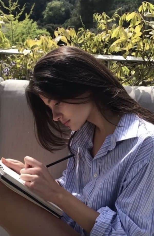 Woman writing in a notebook outdoors, surrounded by greenery, enjoying a peaceful afternoon.