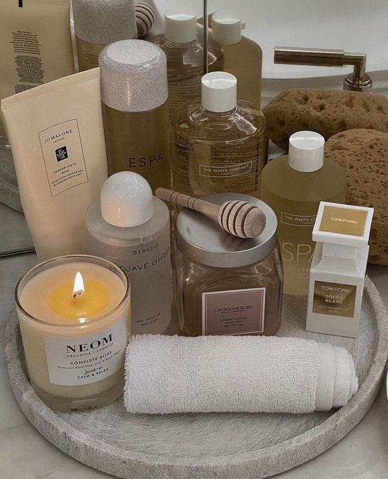 Luxurious bath essentials on a tray with a candle, skincare products, and wooden honey dipper for a relaxing spa experience.