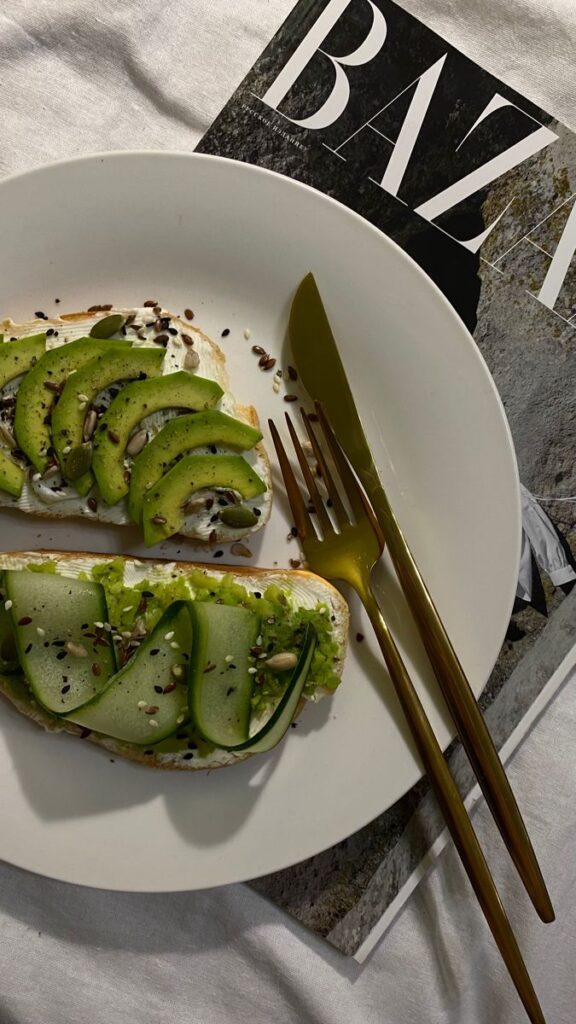 Avocado toast with seeds on a white plate, gold cutlery, magazine background.