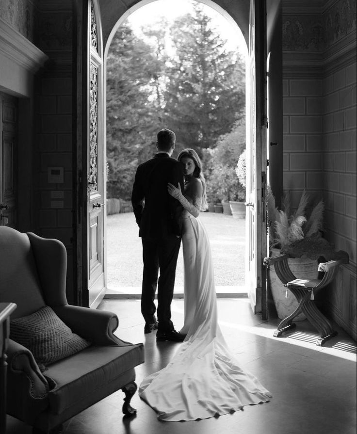 Bride and groom standing in elegant doorway, gazing outside at scenic garden.