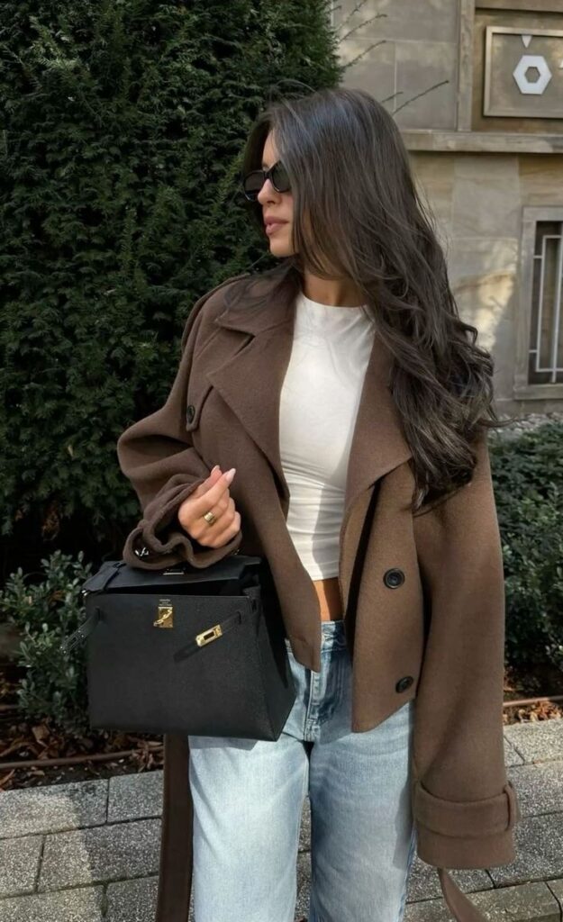 Stylish woman in brown coat with black handbag outdoors, showcasing chic fashion on a sunny day.