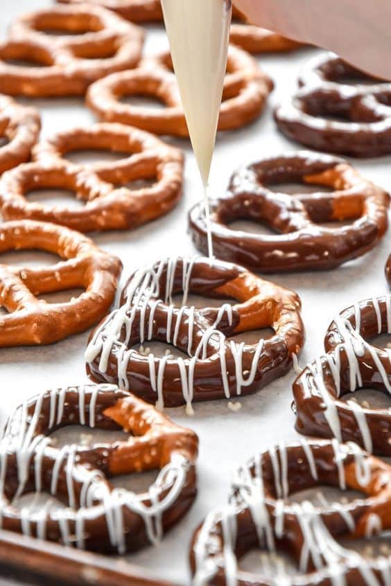 Chocolate-covered pretzels being drizzled with white chocolate on a baking sheet for a delicious treat.