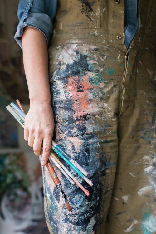 _ 4 Artist in paint-splattered overalls holding paintbrushes, showcasing creativity and artistic expression. | Sky Rye Design Artist in paint-splattered overalls holding paintbrushes, showcasing creativity and artistic expression.