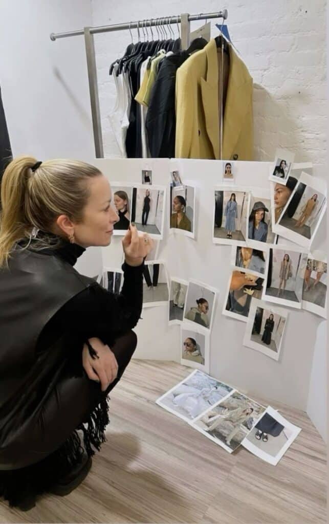 Fashion designer reviewing model photographs and clothing rack for a runway show preparation.
