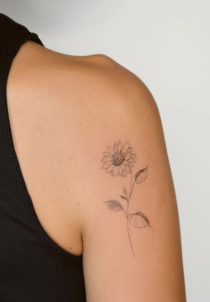 Minimalist sunflower tattoo on upper arm with black tank top.