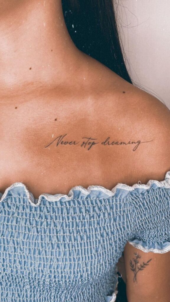 Shoulder tattoo reading 'Never stop dreaming' on person wearing a blue off-shoulder top.
