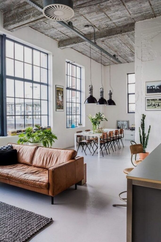 Spacious modern loft with leather sofa, dining table, large windows, and industrial decor elements.