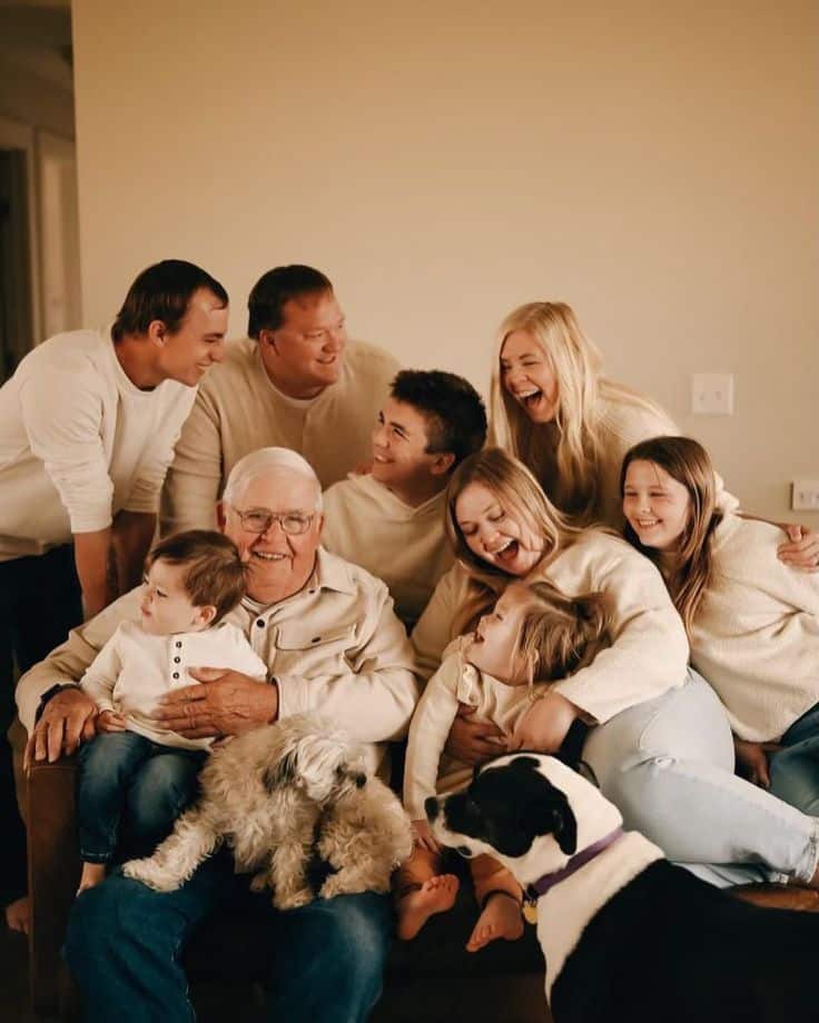 Multigenerational family enjoying a joyful moment with pets on the couch, dressed in cozy attire.