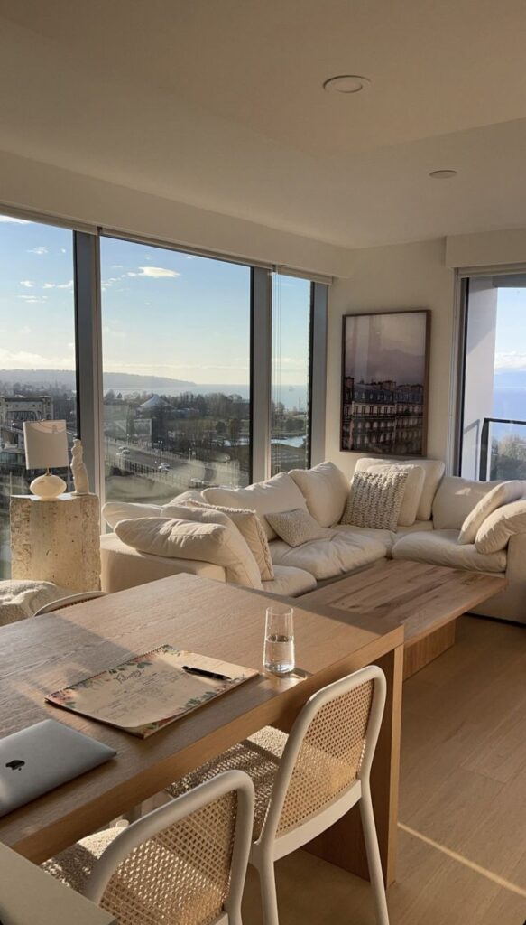 Modern living room with large windows, a cozy white sofa, and a wooden table set in a bright, airy interior.