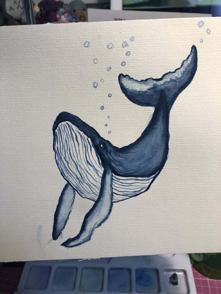 Watercolor painting of a whale with bubbles, showcasing a creative marine art illustration on textured paper.