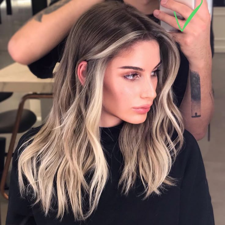 Woman with stylish blonde balayage hair in a salon setting, showcasing modern hair color trend.