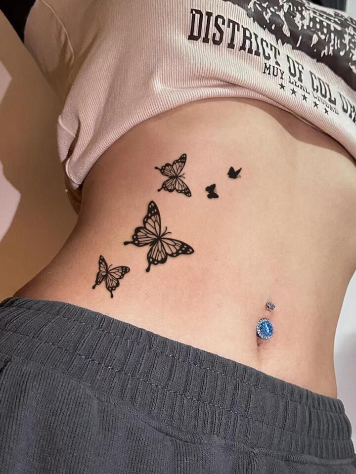417a6c01-4c49-4e8a-aa46-eedfe98054a4 Butterfly tattoos on waist with a blue belly piercing, wearing a cropped top and gray pants. | Sky Rye Design Butterfly tattoos on waist with a blue belly piercing, wearing a cropped top and gray pants.
