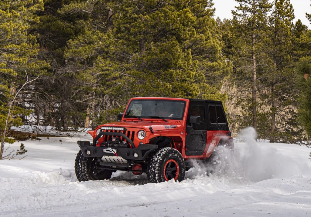 Red off-road vehicle driving through snowy forest terrain.