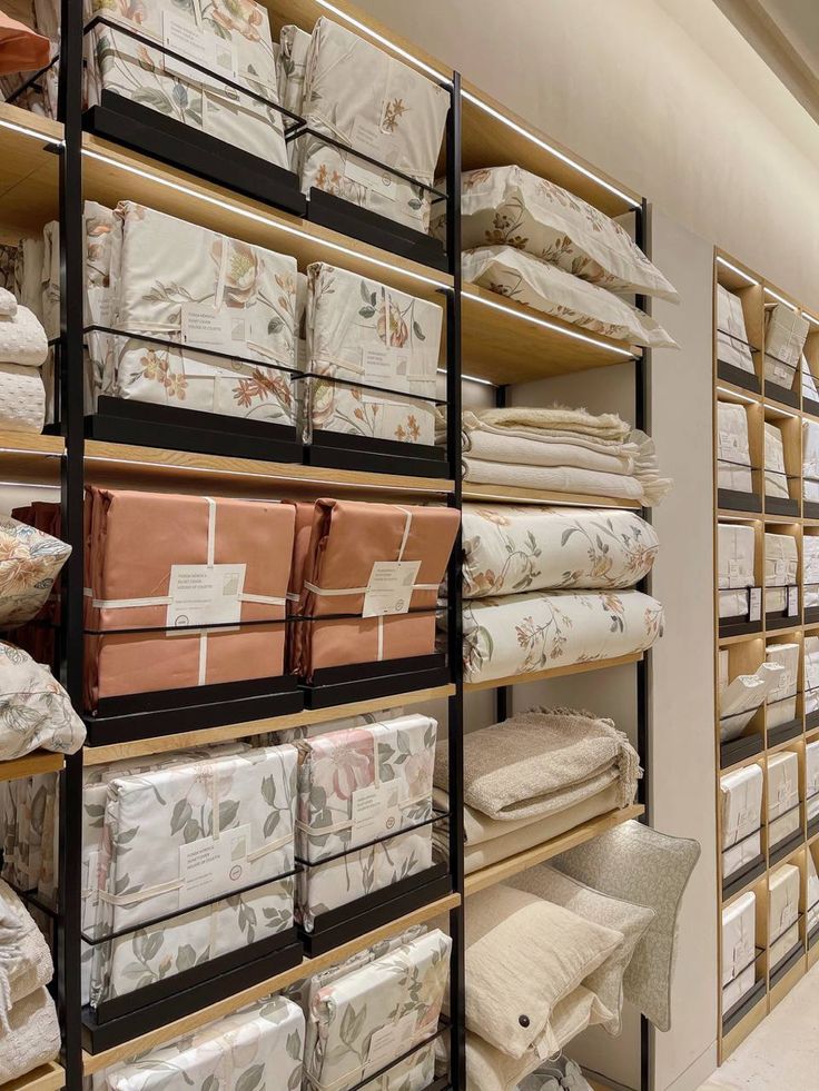 Shelves displaying neatly folded floral and plain bedding sets in a home store, showcasing stylish bedroom decor options.