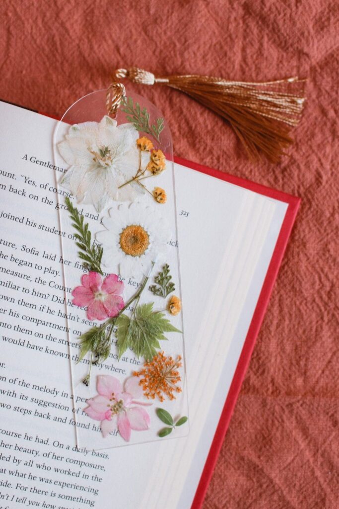 Floral bookmark with pressed flowers on open book, resting on a textured coral fabric.