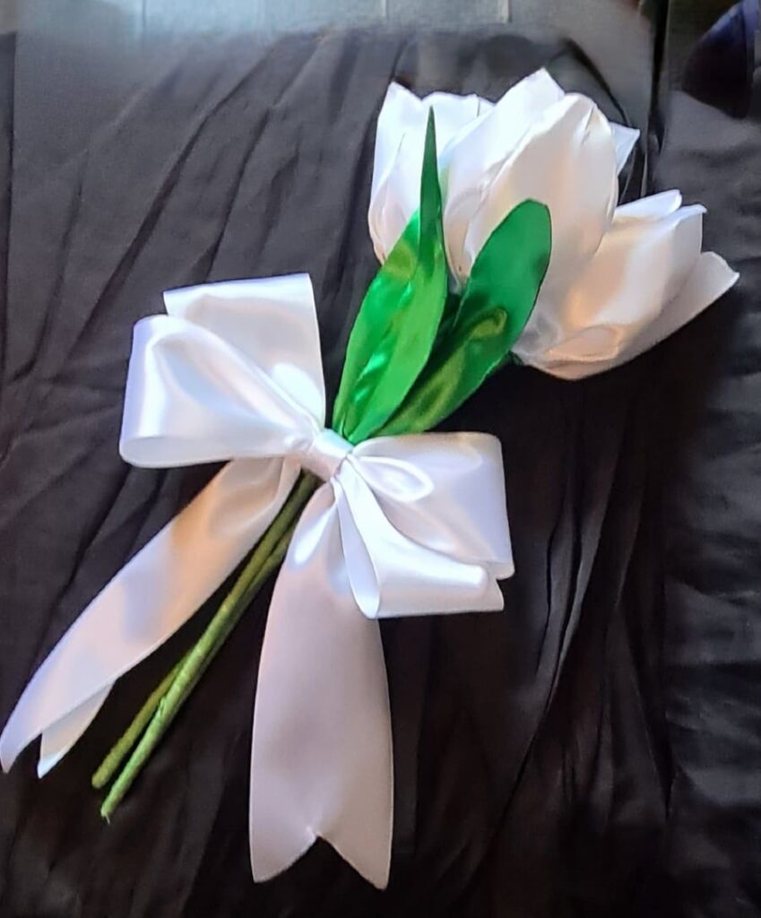 White fabric tulip bouquet with green leaves and a large white bow on dark fabric background.