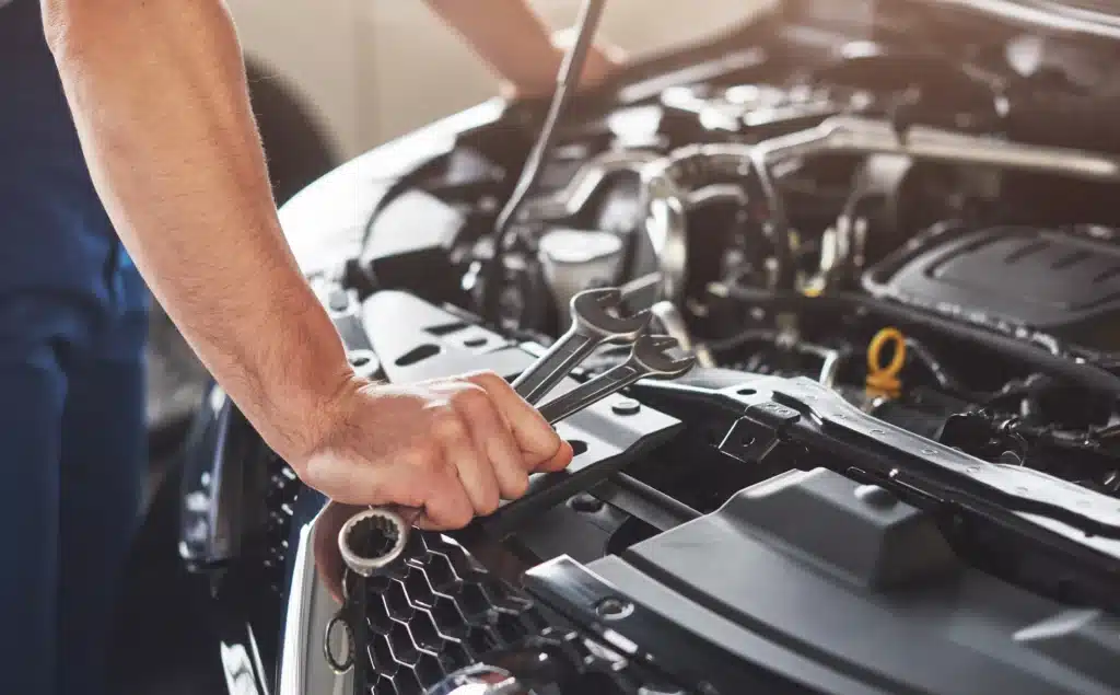 Mechanic using wrenches to repair car engine, close-up view of hands and tools in automotive workshop.