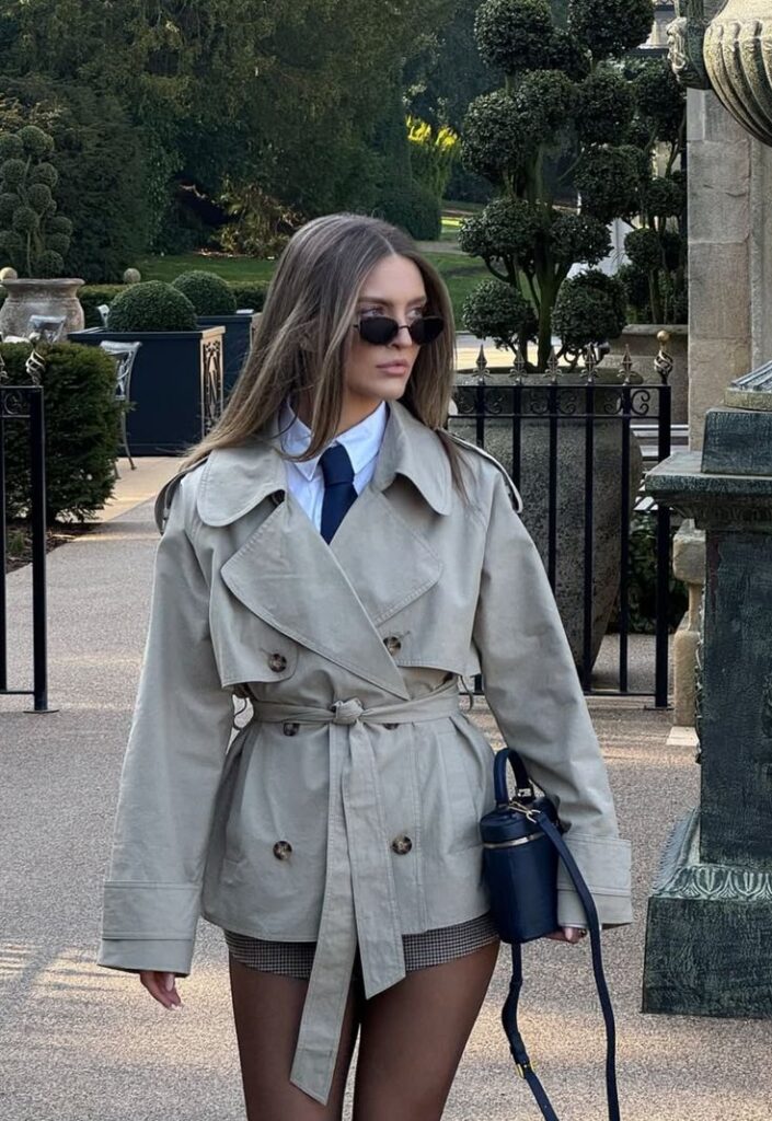 Fashionable woman in trench coat and sunglasses walking in park, elegant and stylish outdoor look.