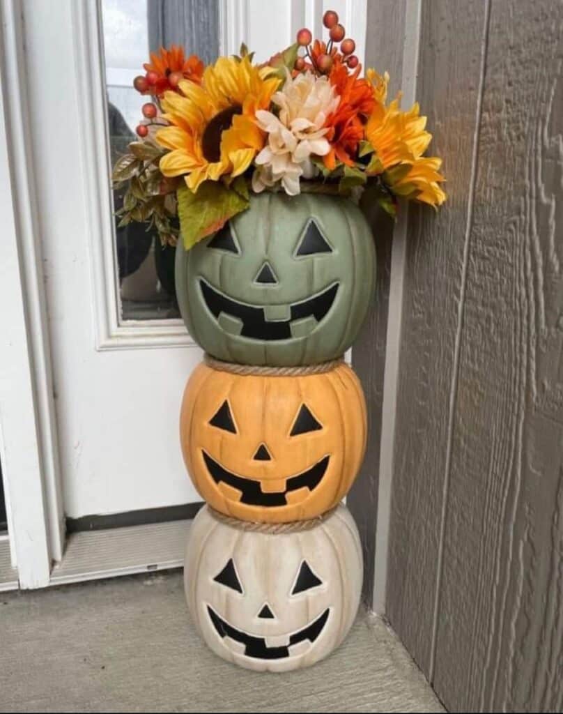 Stacked pumpkin planters with autumn flowers, decorating a porch for fall ambiance and Halloween charm.