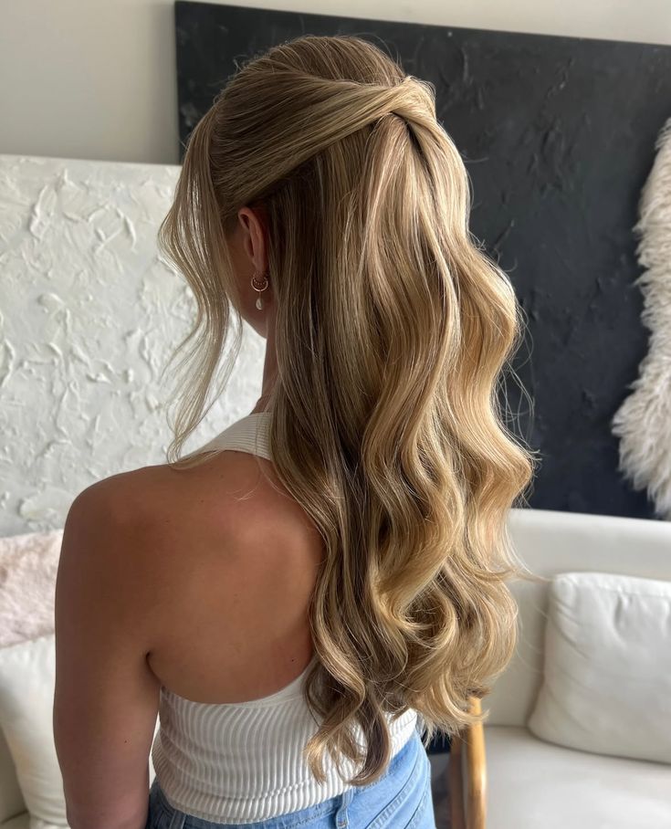 Blonde woman with wavy hair styled in a half-up twist, wearing a white top and jeans, back view.