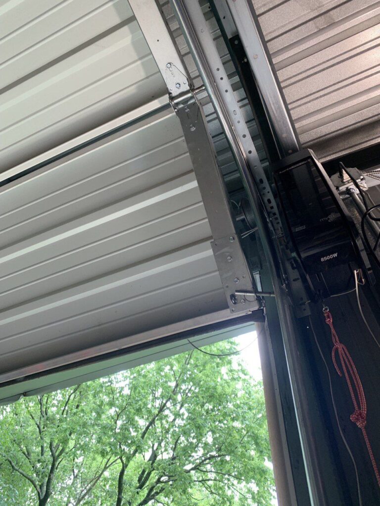 Open garage door partially revealing a green tree outside, metal framework visible inside.