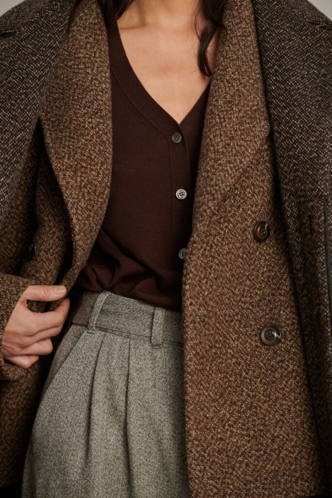 Stylish woman in a brown coat and sweater with grey high-waisted trousers, showcasing autumn fashion.