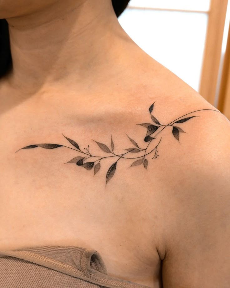 Elegant leafy branch tattoo on shoulder above collarbone, showcasing minimalist style and intricate detail.