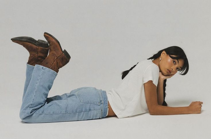 Woman in casual outfit with jeans and boots lying on the floor, white background.