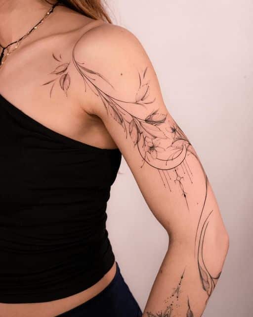Floral arm tattoo with crescent moon design on a person wearing a black top, showcasing intricate line art detail.
