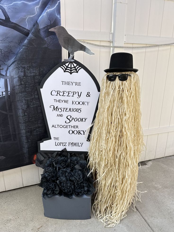 Halloween decor with tombstone, raven, and figure in glasses and hat. They're creepy & kooky, sign reads.