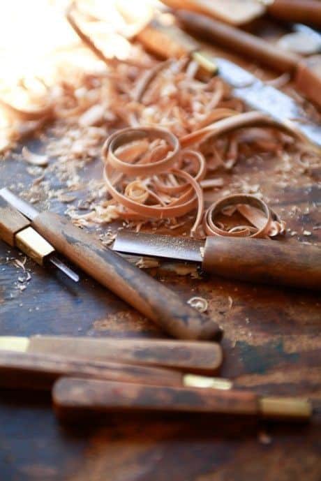 _ 5 Wood carving tools and wood shavings on a workshop table, highlighting intricate woodworking craftsmanship. | Sky Rye Design Wood carving tools and wood shavings on a workshop table, highlighting intricate woodworking craftsmanship.