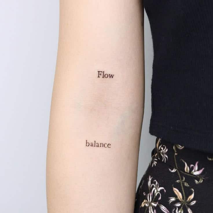 Tattoo of the words Flow and balance on a person's arm, with floral-patterned clothing in view.