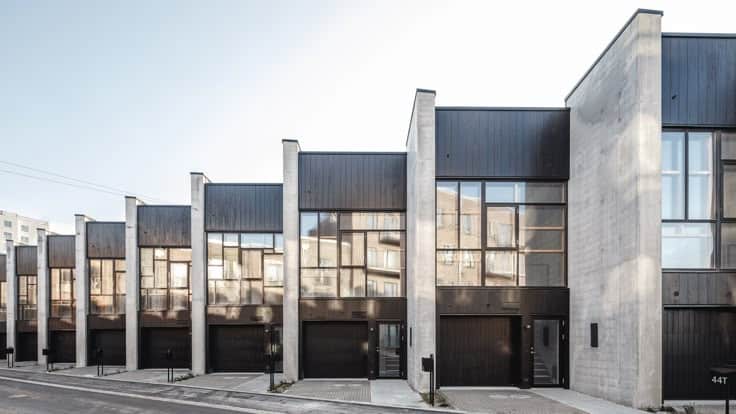 Modern row of minimalist townhouses with large windows, sleek design, and concrete details under a clear sky.