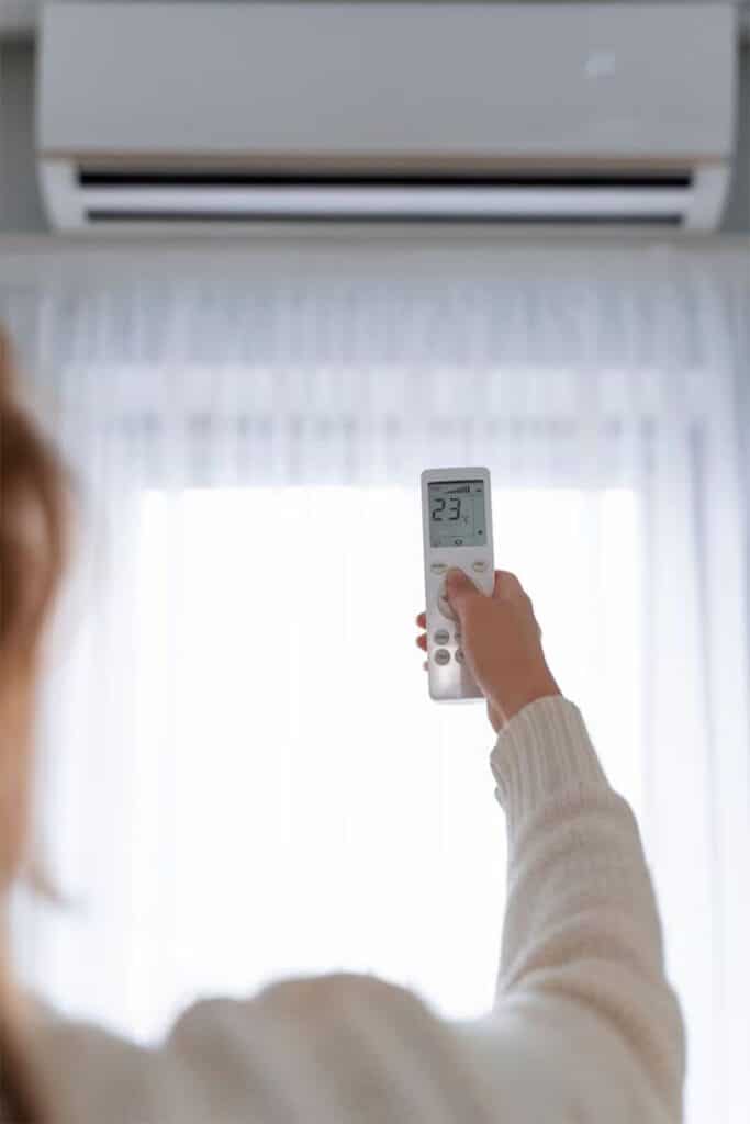 Person adjusting air conditioner with remote control in a bright room.