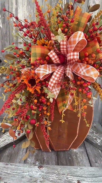 Autumn floral arrangement with vibrant orange, red flowers, and plaid ribbon in a pumpkin vase on rustic wood background.
