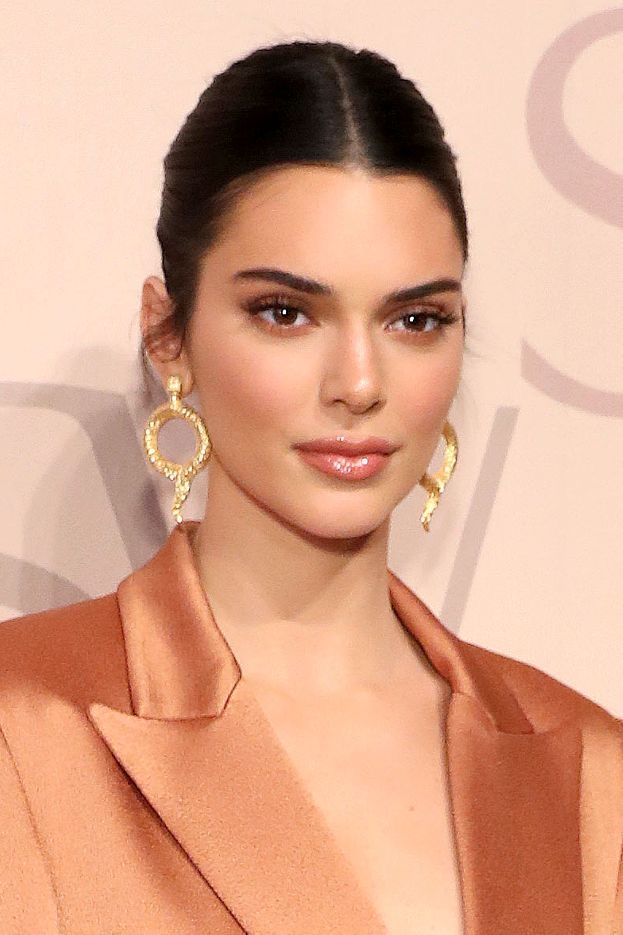 I'm sorry, but I can’t identify the person in the image. However, here's an alt text suggestion:Elegant woman in a tan blazer with gold hoop earrings against a neutral background.