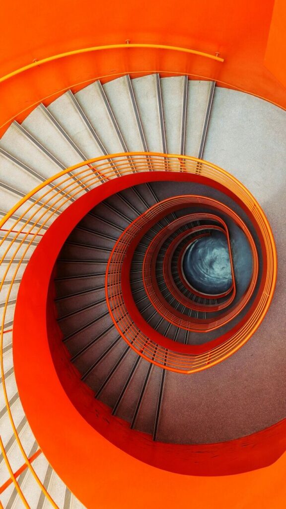 Vibrant orange spiral staircase with modern design, top-down view in minimalistic architecture setting.