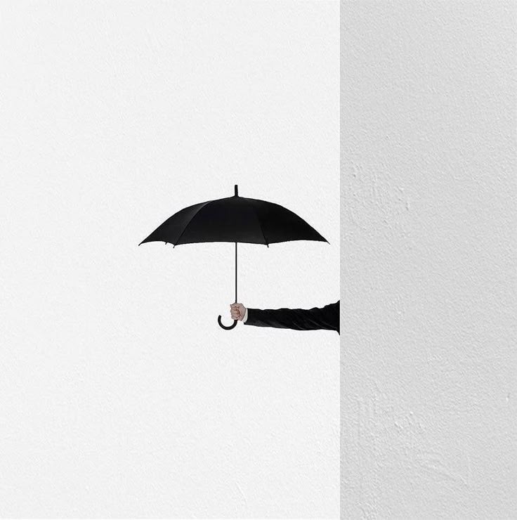 Arm holding black umbrella against white wall, minimalist art concept.