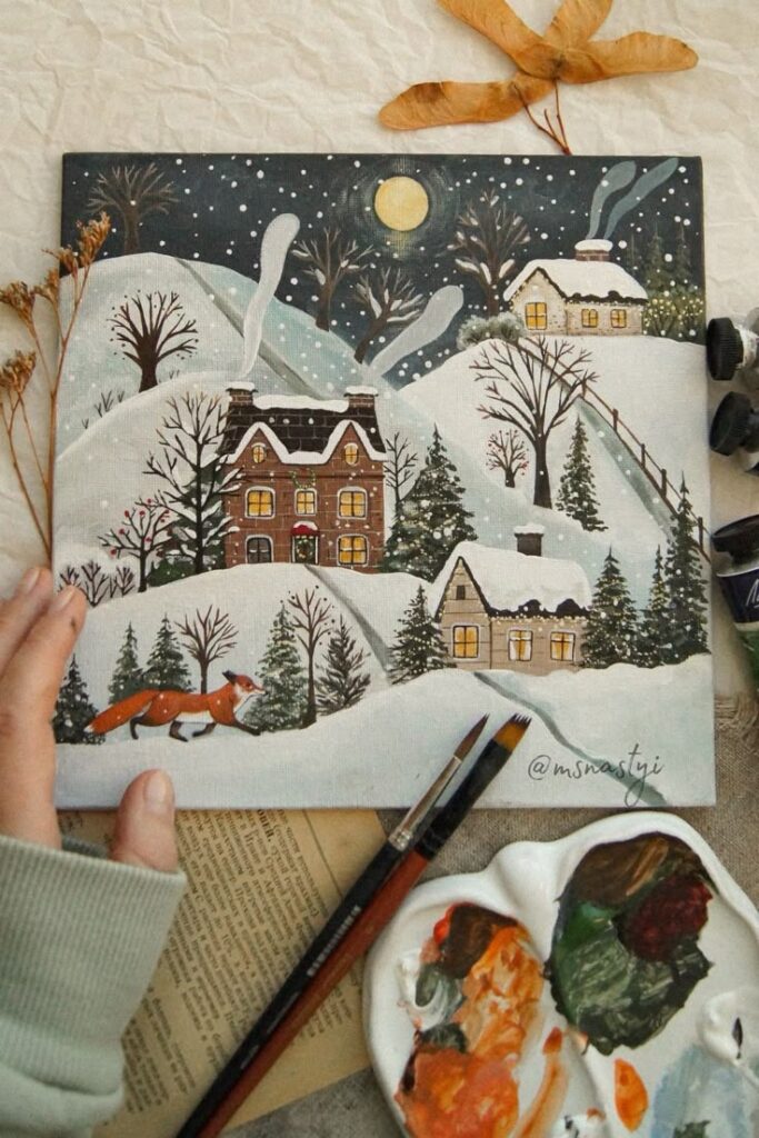 565f21c9-e3a6-45dc-a6ff-1fe6cc5ae29c Snowy village painting with fox and cozy cabins, full moon night, artist's hand, brushes, and paint palette nearby. | Sky Rye Design Snowy village painting with fox and cozy cabins, full moon night, artist's hand, brushes, and paint palette nearby.