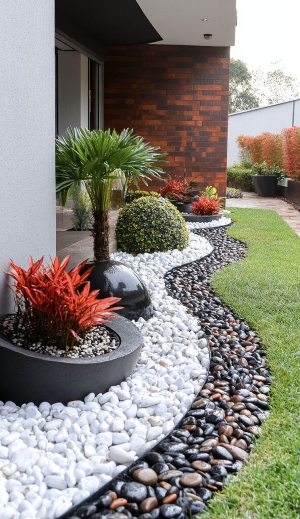 Modern landscaped garden with vibrant red and green plants, surrounded by white and dark decorative stones.