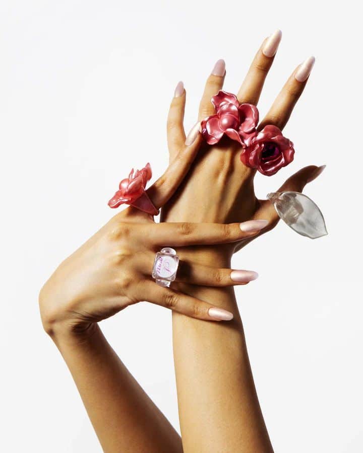 Hands showcasing unique, artistic rings with floral designs on manicured fingers against a white background.