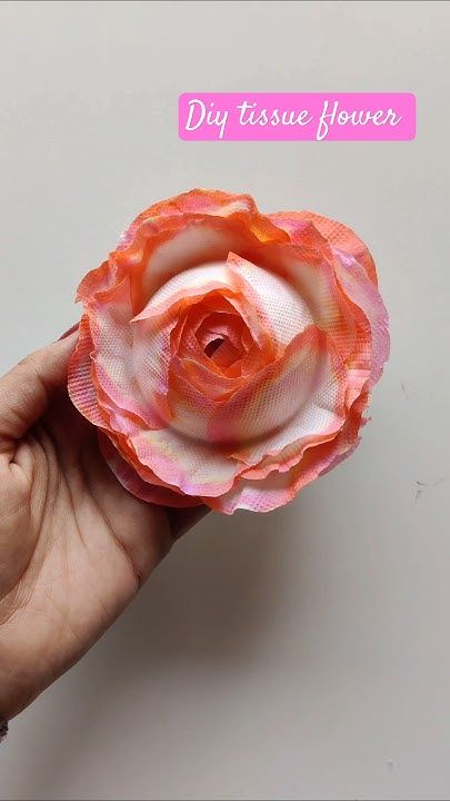 Hand holding a pink and orange DIY tissue paper flower against a white background.