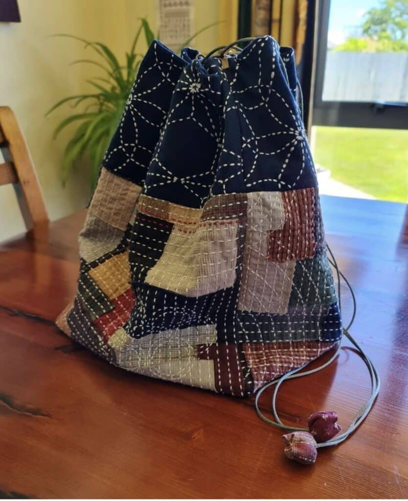 Patchwork drawstring bag with intricate stitching on a wooden table, near a window with outdoor greenery.